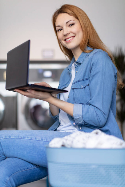 nice woman checking the laundry machine while work on laptop - Фото, зображення