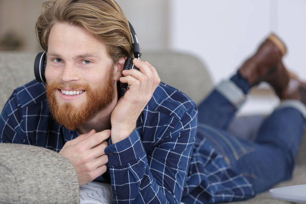 happy man lying on couch at home wearing headphones - Photo, Image