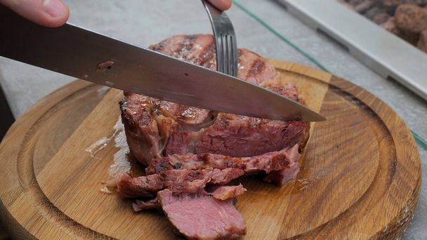 Close up shot of a juicy freshly grilled steak straight from the grill being cut with fork and knife on kitchen table - Photo, Image