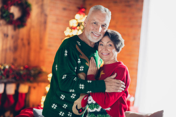 Photo of sweet positive couple hugs together smiling wear cozy warm ugly red green sweaters fell love enjoy xmas tradition home decor indoors. - Photo, Image