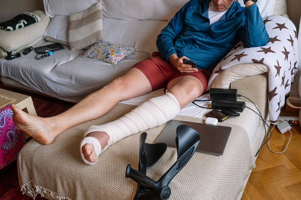 Homem ferido com o pé enfaixado usando um smartphone. - Foto, Imagem