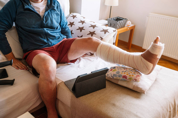 Yaralı, ayağı bandajlı bir adam tablet kullanıyor.. - Fotoğraf, Görsel