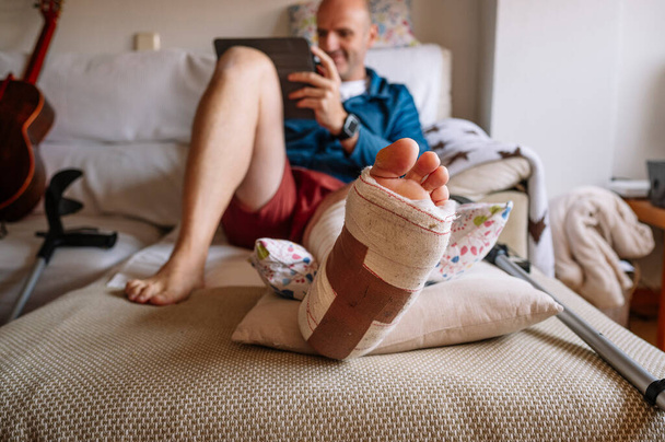 Yaralı, ayağı bandajlı bir adam tablet kullanıyor.. - Fotoğraf, Görsel