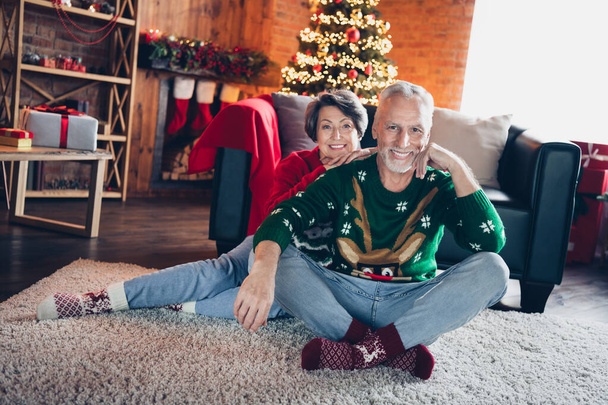 Full body portrait of two cheerful satisfied aged people sit carpet floor cuddle fairy christmastime miracle indoors. - Photo, Image