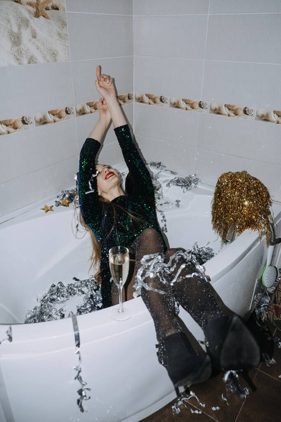 New Years Party Birthday celebration. Happy young woman in evening dress sitting in the bathtub drinking champagne and having fun - Foto, afbeelding