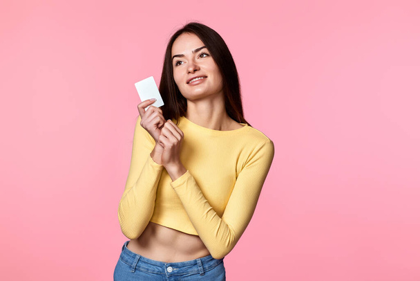 young woman in yellow clothes holding plastic credit card isolated on pink background - Foto, immagini