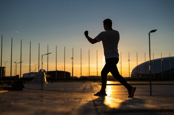 A man trains boxing at sunset outdoors - Valokuva, kuva