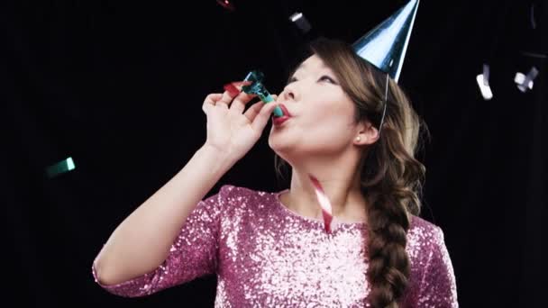 Party, konfety a žena na oslavu narozenin nebo svátků s kloboukem a rohem ve studiu. Slavit, štěstí a asijské dáma slaví na akci izolované černým pozadím - Záběry, video