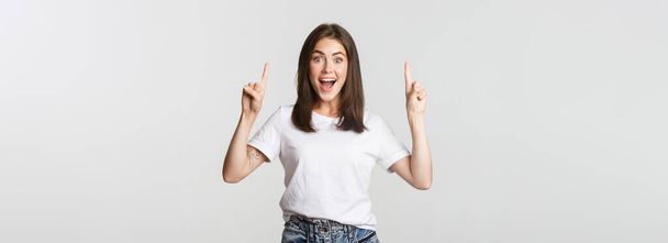 Attractive smiling brunette girl pointing fingers up, showing logo. - Foto, imagen