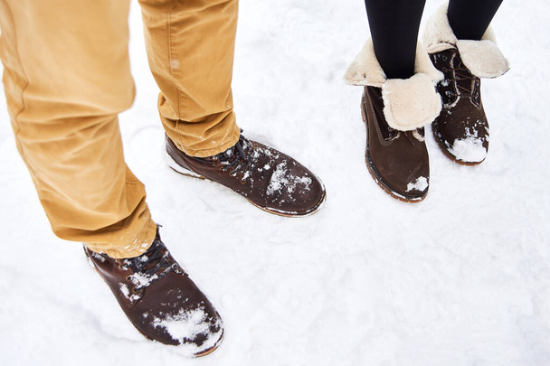 couple in love wear brown boots stay and walk on white fresh snow in winter. winter comfortable shoes - Photo, Image
