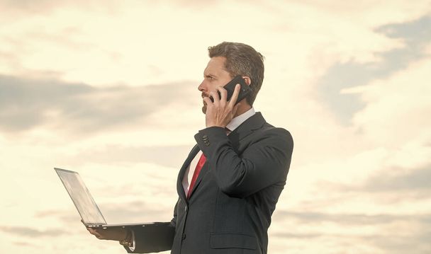 άνδρας με κοστούμι μιλάει στο τηλέφωνο και να κρατήσει το φορητό υπολογιστή. - Φωτογραφία, εικόνα