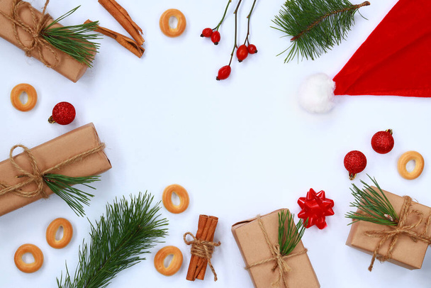 Keret karácsonyi kiegészítők fehér háttér a központban, fehér háttér. Piros sapka, ajándékdoboz, lucfenyő ág, bagel, fahéjas tubus, csipkebogyó és karácsonyi dekoráció - Fotó, kép