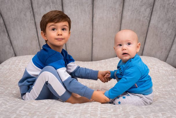 Двоє маленьких хлопчиків сидять разом у яскравому ліжку. Розважатися Концепція маленьких дітей
 - Фото, зображення