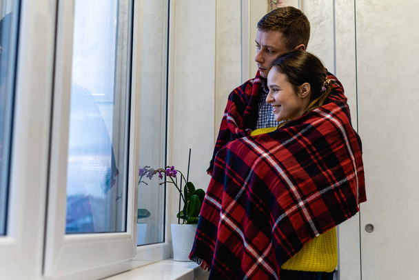 glücklich und verliebt stehen junge Männer und Mädchen am Fenster, umarmt, mit einer Decke bedeckt, kalt. Selektiver Fokus - Foto, Bild