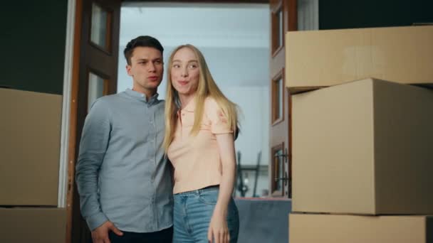 New cheerful tenants standing in rented apartment looking living room interior. Happy young family entering flat full of packed carton boxes. Lovely homeowners smiling moving in mortgage house. - Footage, Video