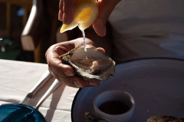 Mujer joven en vestido blanco come ostras frescas creuze vivo con cebolla marinada, mariscos en restaurante francés - Foto, Imagen