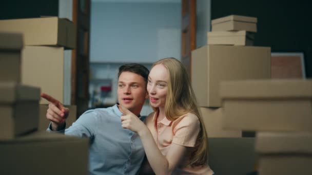Two happy homeowners discussing interior design sitting on floor new house living room surrounded packed carton boxes close up. Young married couple enjoying moving in modern purchased apartment. - Footage, Video