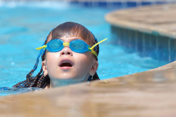 Young child girl in goggles learning to swim in blue pool water outdoors. Summer recreation activity concept. - Photo, Image