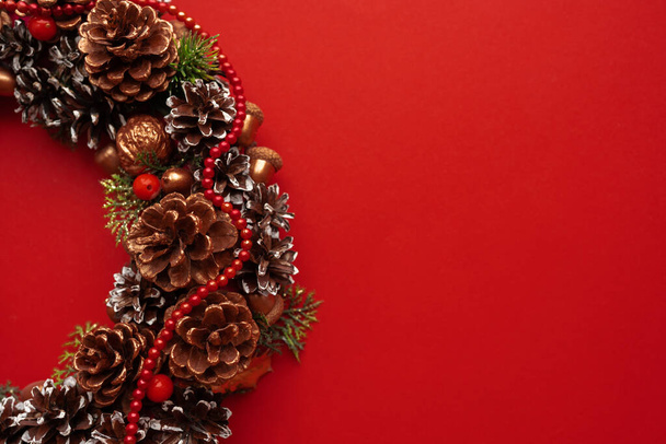 Karácsonyi dekoráció fenyőtobozokkal, díszített karácsonyi koszorú vörös háttérrel. Karácsonyi hangulat - Fotó, kép