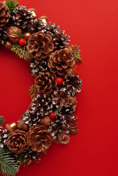 Świąteczna dekoracja szyszkami sosnowymi, ozdobiony świąteczny wieniec na czerwonym tle. Świąteczny nastrój - Zdjęcie, obraz