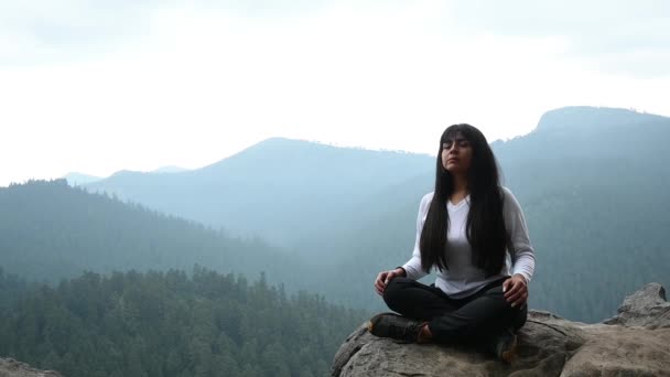 Mujer joven meditando y respirando en la cima de una montaña y bosque - Metraje, vídeo