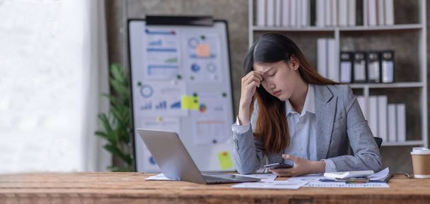 Молодые деловые азиатки испытывают стресс во время работы на ноутбуке Уставшая азиатская деловая женщина с головной болью в офисе, чувствующая грусть или тошноту на рабочем месте. - Фото, изображение