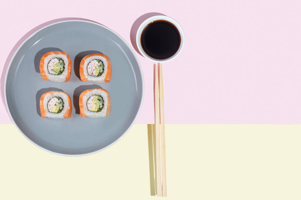 Sushi japonais au saumon, dragon roule sur un fond jaune-rose vif. Pop art. Snacks savoureux sur une assiette grise et baguettes. Alimentation traditionnelle asiatique - Photo, image