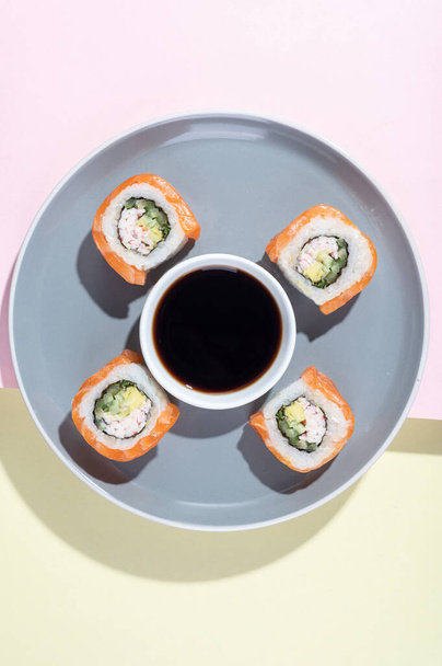 Ιαπωνικό σούσι με σολομό, ρολό δράκου σε λαμπερό κίτρινο-ροζ φόντο. Ποπ αρτ. Νόστιμα σνακ σε γκρι πιάτο και ξυλάκια. Ασιατικό παραδοσιακό φαγητό - Φωτογραφία, εικόνα