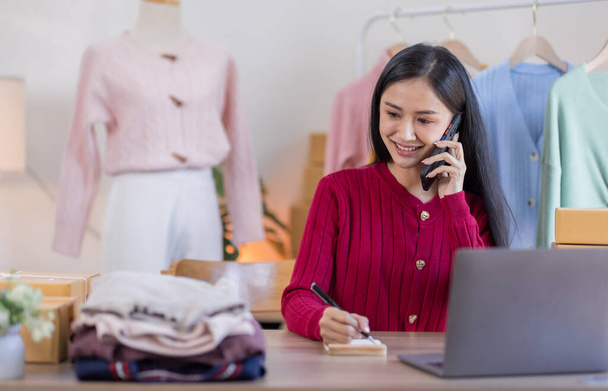 Mujeres asiáticas PYME que venden ropa en línea, Ella está respondiendo a las preguntas de los clientes por teléfono y portátil en casa, Empresario de pequeñas empresas de partida independiente, Negocios en línea, concepto de PYME. - Foto, Imagen