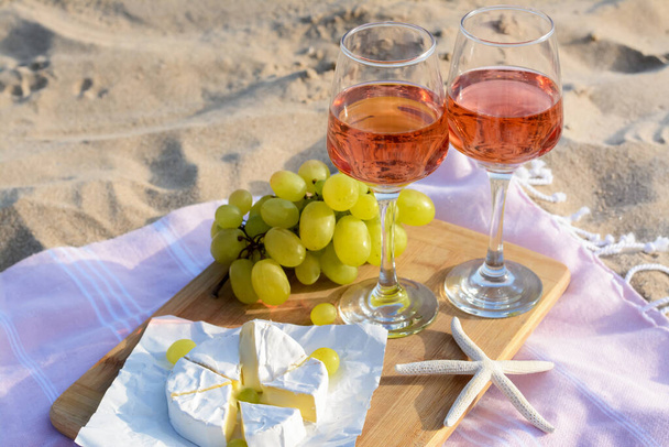 Glasses with rose wine and snacks for beach picnic on sand outdoors - Foto, Bild