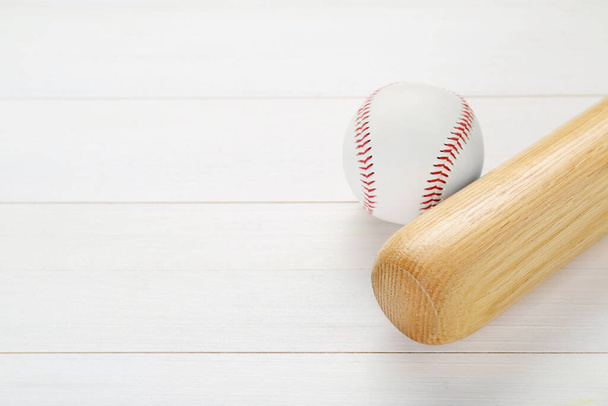 Baseball bat and ball on white wooden table, above view with space for text. Sports equipment - Photo, image