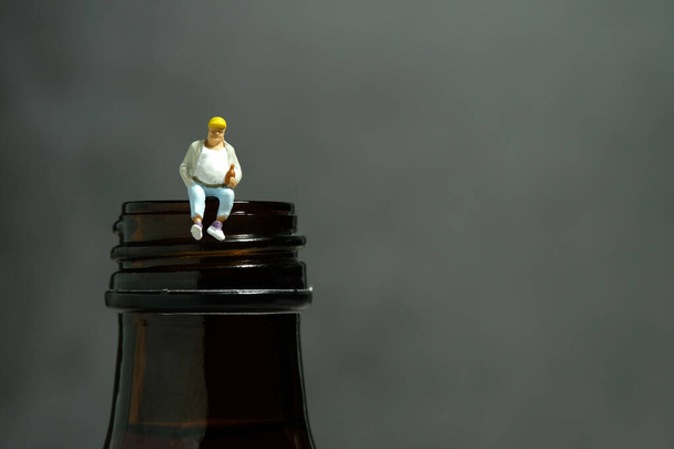 Miniatyyri ihmiset lelu kuva valokuvaus. Stressaantunut ja masentunut lihava mies, joka istuu olutpullon yläpuolella. Kuva kuva - Valokuva, kuva
