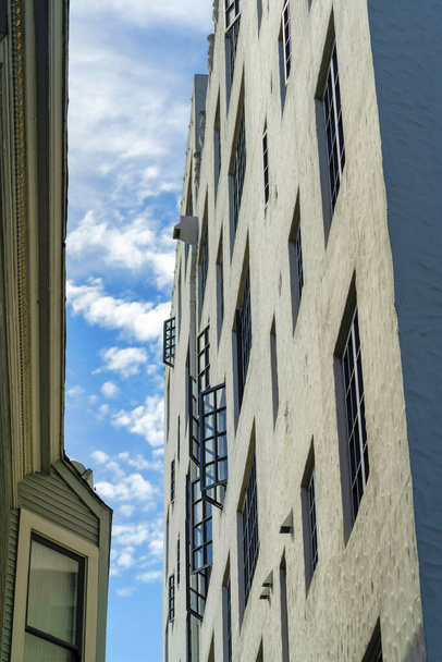 Σύγχρονη πολυκατοικία και σοκάκι τρόπο με μαύρη προφορά ζωγραφισμένα παράθυρα κάποια ανοικτή στο εξωτερικό του κτιρίου στο μεσημέρι ήλιο. Δεύτερο κτίριο αριστερά στη σκιά με διακοσμητική πρόσοψη παλαιού στυλ με ουρανό. - Φωτογραφία, εικόνα