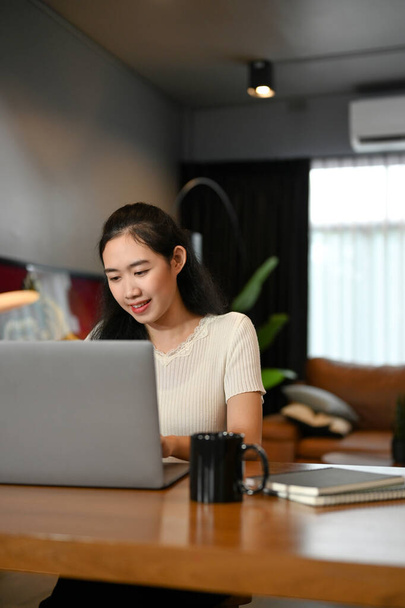 Retrato, bonita e atraente jovem asiática mulher na sala de estar usando computador portátil para gerenciar suas tarefas. - Foto, Imagem