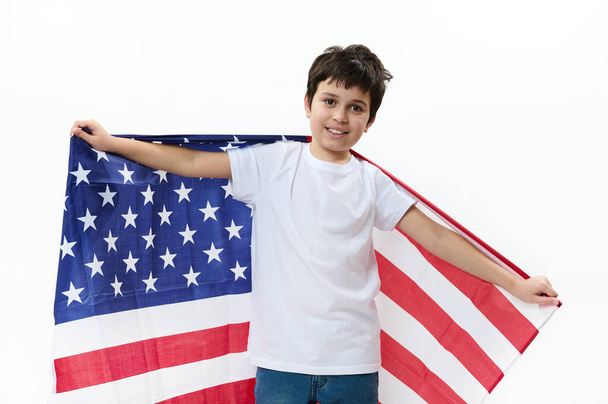 Happy American preteen boy in casual t-shirt and denim jeans, carries USA flag, celebrates Independence Day, July 4th. Citizenship, immigration, emigration, winning green card lottery, freedom concept - Photo, image