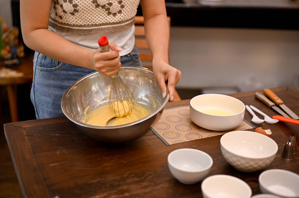 Una femmina fa un cupcake fatto in casa nella sua cucina di casa, sbattendo il burro ammorbidito, zucchero, uova e farina insieme nella ciotola di miscelazione. immagine ritagliata - Foto, immagini
