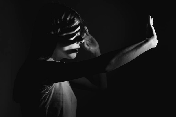 The girl covers her face with her hands from the bright light in the dark, light and shadows - Fotó, kép