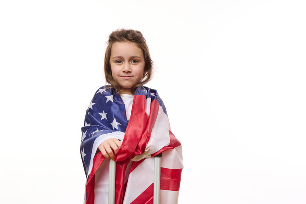 Amerikan bayrağı ve bavulu olan mutlu bir Amerikalı kızın beyaz arka planda izole edilmiş portresi. Vatandaşlık, göç, göç, Amerika 'da eğitim, yeşil kart piyangosunu kazanmak ve özgürlük kavramı - Fotoğraf, Görsel