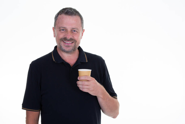 красивий чоловік в чорній сорочці поло тримає чашку кави гарячий напій, посміхаючись розслабляючись на білому тлі
 - Фото, зображення