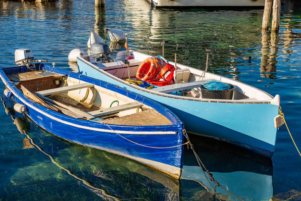 Close-up van twee kleine houten vissersboten afgemeerd in de kleine haven van het dorp Malcesine, toeristische badplaats aan de kust van het Gardameer. provincie Verona, Veneto, Italië, Zuid-Europa. - Foto, afbeelding