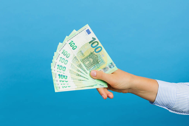 Woman's hand holding hundred euros banknotes isolated on blue background. Euro money, cash banknotes - Фото, зображення