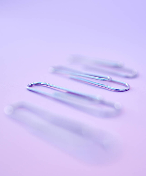 Row, paper clips and office stationery for paperwork in a studio with a purple background. Work supplies, equipment and steel wire clips in a line to organize or hold document, report or form sheets - Foto, Bild