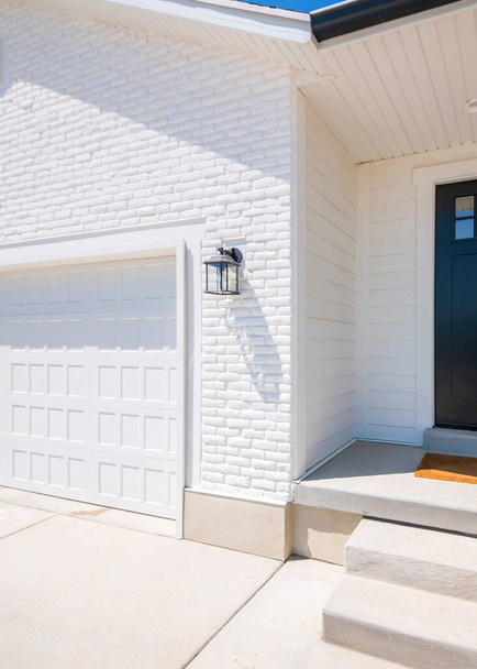 Vertikální fasáda domu s bílým zevnějškem a černými předními dveřmi se sklem, dveřní zvonovou kamerou a zamykatelnou skříní. Domácí exteriér s bílým vinylovým břichem a cihlovým vzorem vlečky a připojená garáž - Fotografie, Obrázek