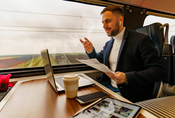 Empresario viajando en tren, hablando para una videollamada a través de computadora portátil, discute nuevas ideas de proyecto - Foto, imagen