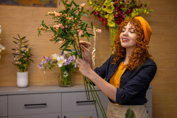 Working with flowers. Ginger girl sorting flowers and looking contented - Foto, Imagem