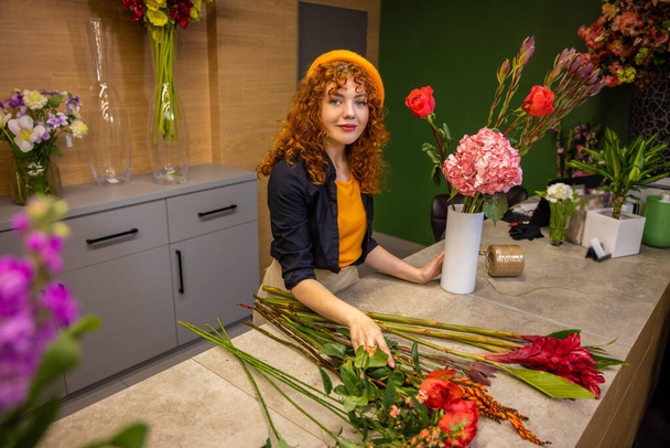 Working with flowers. Ginger girl sorting flowers and looking contented - 写真・画像