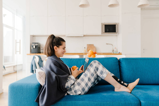 Fiatal nő protézis segítségével tabletta számítógép és eszik alma kanapén otthon - Fotó, kép
