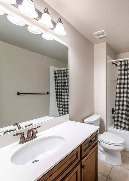 Verticale Traditionele badkamer interieur met geruite zwart-wit douchegordijn. Er is een wastafel aan de linkerkant met spiegel in de buurt van het toilet aan de overkant van de handdoek bar aan de rechterkant. - Foto, afbeelding