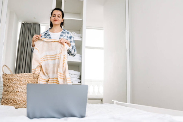 Young woman wearing pajama using laptop while doing housework at home - Фото, зображення