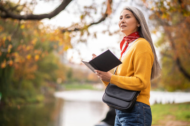 Autumn inspiration. Beautiful mature woman with a notebook in hands looking inspired - Photo, Image